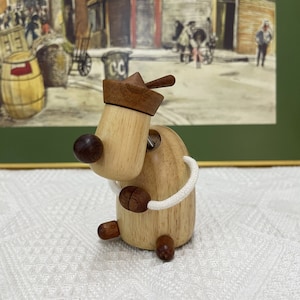 Könnte beinhalten: Ein hölzerner Spielzeug-Hund, der einen braunen und weißen Matrosenhut trägt. Der Hund sitzt auf einer weißen Oberfläche.