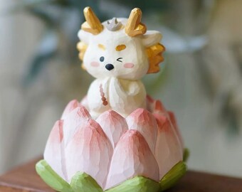 May include: A white wooden figurine of a dragon sitting on a pink and green lotus flower. The dragon has gold accents and a crown.