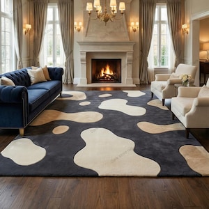 Puede incluir: Una alfombra grande, gris oscuro, con formas abstractas de color crema. La alfombra está colocada en un salón con un sofá azul, sillones blancos, una chimenea y suelos de madera. La habitación está bien iluminada con luz natural.