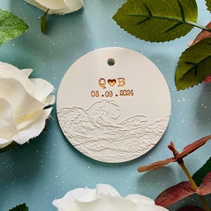 May include: White ceramic ornament with a wave design and the text "Q♥B 08.09.2024" in gold.