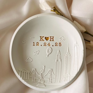 Könnte beinhalten: Weiße Keramik-Ring Schale mit einer goldenen Inschrift "K♥H 12.24.25" und einem erhabenen Design der New Yorker Skyline.