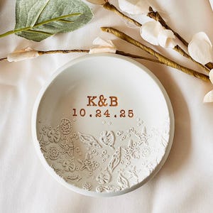 May include: White ceramic ring dish with a seashell design and the inscription "K&B 10.24.25" in gold lettering.