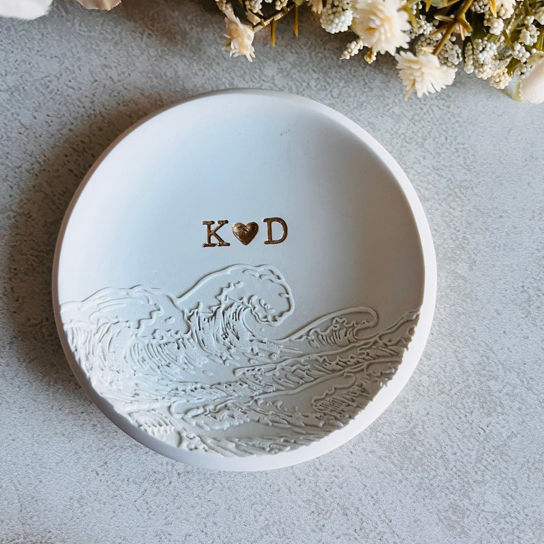 May include: White ceramic ring dish featuring a wave design and the initials "K&hearts;D" in gold lettering.