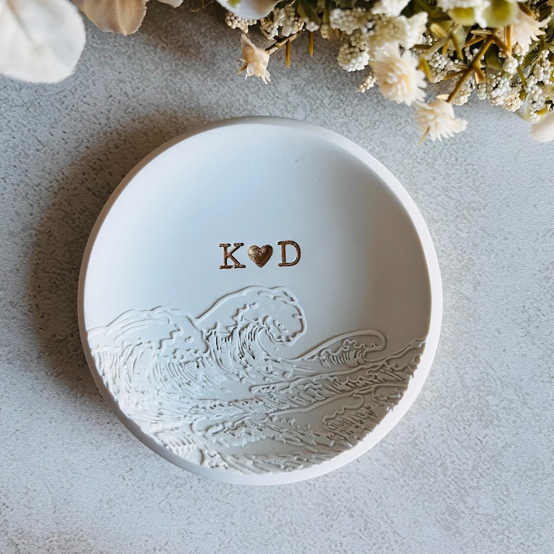 May include: White ceramic ring dish featuring a wave design and the initials "K&hearts;D" in gold lettering.