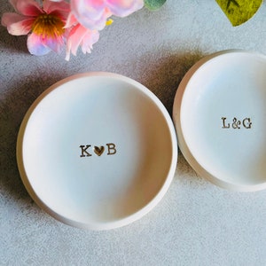 May include: Two white ceramic ring dishes with gold lettering. One dish says "K ♥ B" and the other says "L & G".