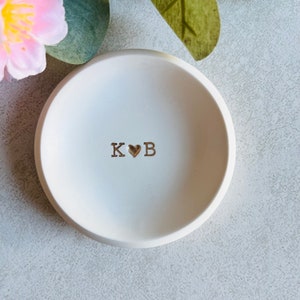 May include: White ceramic ring dish with the initials "K ♥ B" in gold lettering.