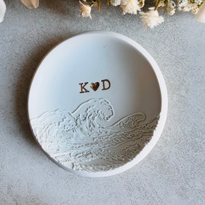 May include: White ceramic ring dish featuring a wave design and the initials "K&hearts;D" in gold lettering.