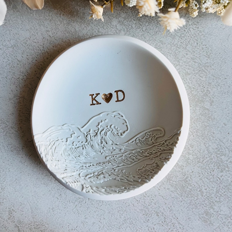May include: White ceramic ring dish featuring a wave design and the initials "K&hearts;D" in gold lettering.