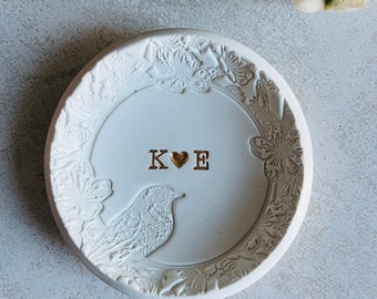 Puede incluir: Plato de cerámica blanco para anillos con un diseño floral y un pájaro. El plato tiene las iniciales "K ♥ E" en letras doradas.