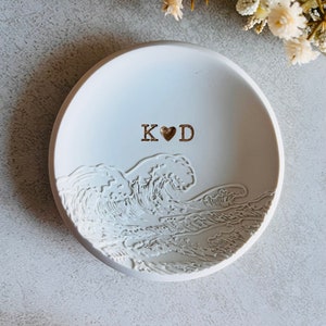 May include: White ceramic ring dish featuring a wave design and the initials "K&hearts;D" in gold lettering.