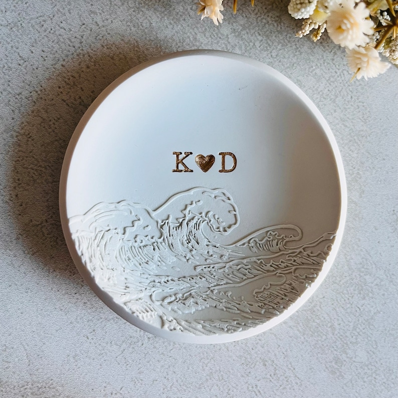 May include: White ceramic ring dish featuring a wave design and the initials "K&hearts;D" in gold lettering.