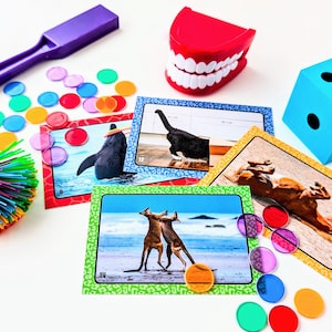 May include: A collection of colorful toys and educational items, including a purple wand, a red set of teeth, a blue die, and several game cards with animal pictures. There are also colorful discs and a spiky ball.