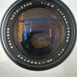 May include: A black Soligor Auto-Zoom camera lens with the specifications 1:4.5 f=75mm-260mm. The lens has a reflective surface and is set against a white background. The lens has the serial number NO. 17524746.