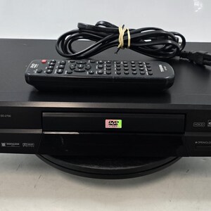 May include: Black Toshiba DVD video player with a remote control and power cord. The DVD player has a disc tray, buttons, and a display. The remote control is black with multiple buttons. The power cord is black and coiled.