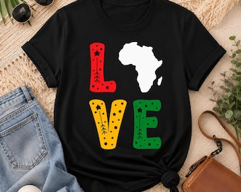 Puede incluir: Una camiseta negra de manga corta con la palabra LOVE impresa en letras grandes. La letra L es roja con estrellas, la letra O es un mapa blanco de África, la letra V es amarilla con estrellas y la letra E es verde con estrellas.