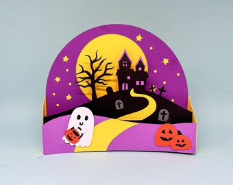 Könnte beinhalten: Ein Halloween-Papier-Diorama mit einem Spukhaus, einem Vollmond und einer kurvenreichen Straße. Ein Geist mit einem Kürbis und zwei geschnitzten Kürbissen sind zu sehen. Die Farbgebung umfasst Lila, Gelb, Schwarz und Orange, was eine gruselige Atmosphäre schafft.