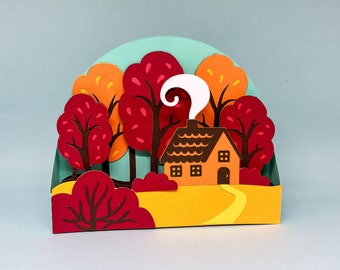Könnte beinhalten: Eine Papierbastel-Szene mit einem kleinen orangenen Haus mit braunem Dach und weißem Rauch aus dem Schornstein. Das Haus ist umgeben von roten und orangenen Bäumen und einem gelben Weg, der zur Haustür führt.