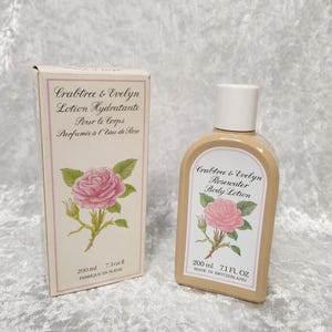May include: A Crabtree & Evelyn Rosewater Body Lotion bottle and box. The beige bottle and box feature a pink rose illustration. The box reads "Lotion Hydratante Pour le Corps Parfumée à l'Eau de Rose". The bottle contains 7.1 fl oz (200 ml) and is made in Switzerland.