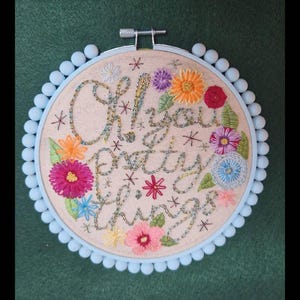 Puede incluir: Arte de aro bordado con la frase "Oh! You Pretty Things" en escritura cursiva, rodeada de coloridas flores bordadas y acentos de estrellas. El aro es azul claro con un ribete de pomp&oacute;n, sobre un fondo verde.