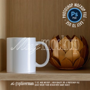 Puede incluir: Maqueta de taza de cerámica blanca en un estante de madera con un objeto decorativo dorado. El texto "Mug mockup" está escrito en blanco en la imagen.