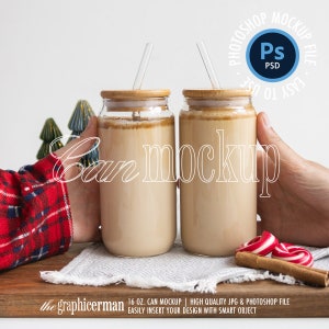 May include: Two glass can mockups filled with a creamy beverage, each topped with a bamboo lid and a clear straw. The image includes the text "Can mockup" and a "PSD" logo. The background features decorative elements and a wooden serving board.