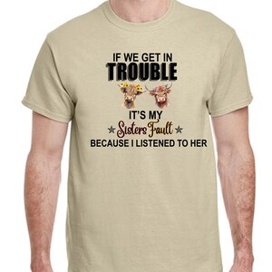 May include: A beige t-shirt with a black graphic print that says "If we get in trouble it's my sister's fault because I listened to her". The graphic also includes two brown and white cows with floral headbands.