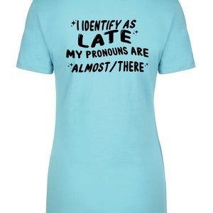 May include: A light blue t-shirt with black text that reads "I identify as late. My pronouns are almost/there."