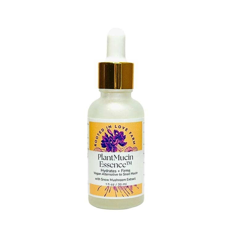 May include: A pearlescent glass bottle with a dropper, featuring a gold cap and a white top. The label reads "PlantMucin Essence" with text indicating it hydrates and firms, with 1 fl oz / 30 ml. The label also includes the words "Rooted in Love Farm". Made with snow mushroom