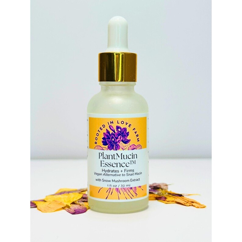 May include: A clear glass bottle of Plant Mucin Essence with a gold dropper top and a yellow label. The label features purple flowers and the text "ROOTED IN LOVE FARM" and "Plant Mucin Essence". The bottle contains 1 fl oz / 30 ml. Hydrates with snow mushroom.