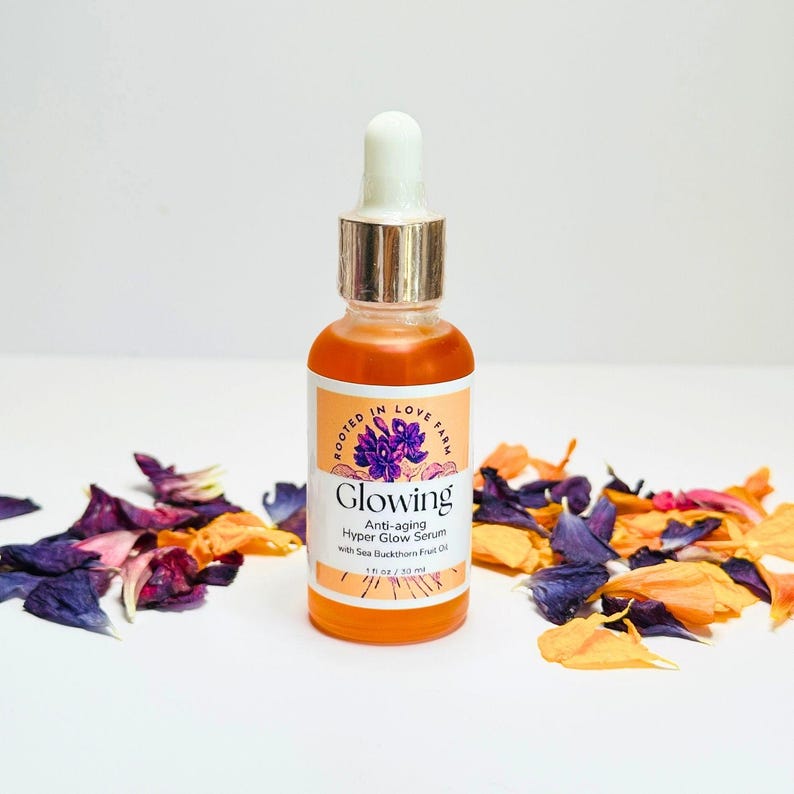 An orange serum in a dropper bottle named “Glowing” with anti aging and wrinkle organic botanicals and clean ingredients for healthy glowing skin.