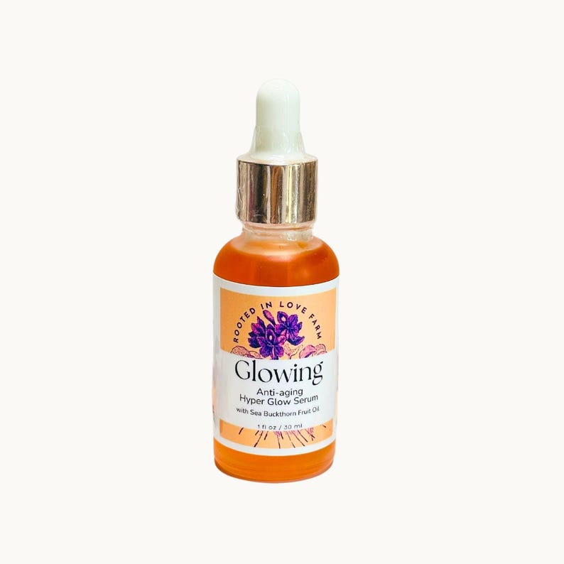 An orange serum in a dropper bottle named “Glowing” with anti aging and wrinkle organic botanicals and clean ingredients for healthy glowing skin.
