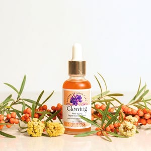 An orange serum in a dropper bottle named “Glowing” with anti aging and wrinkle organic botanicals and clean ingredients for healthy glowing skin.