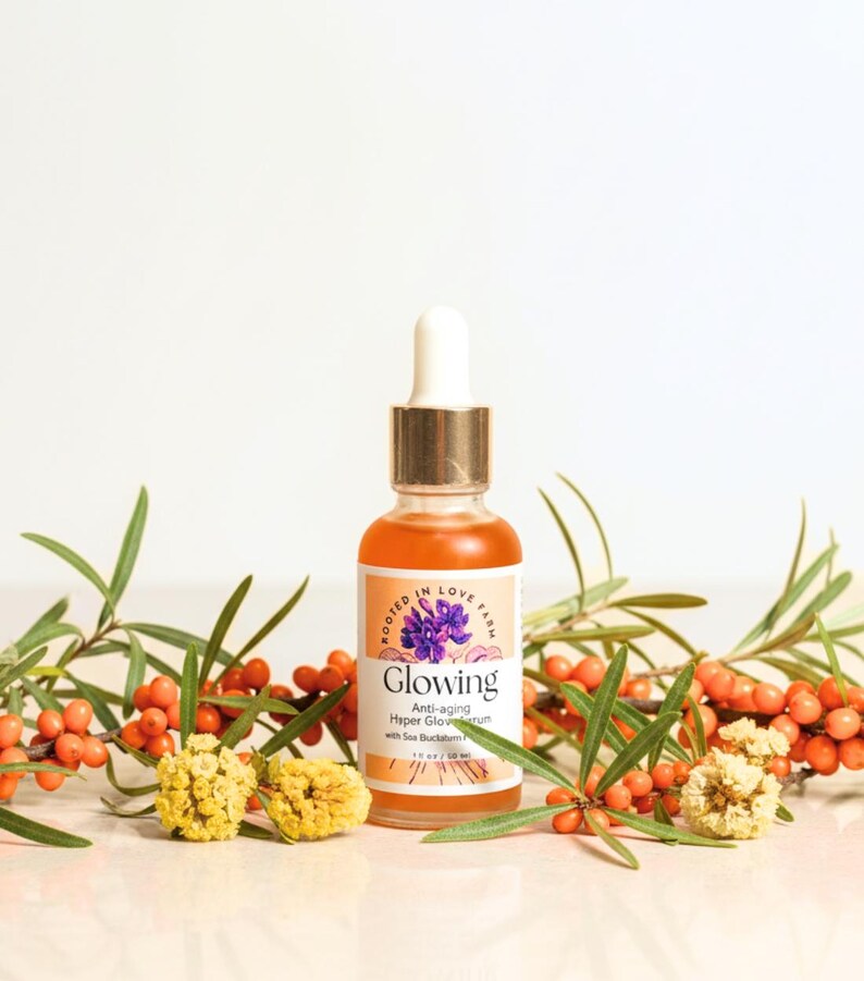 An orange serum in a dropper bottle named “Glowing” with anti aging and wrinkle organic botanicals and clean ingredients for healthy glowing skin.