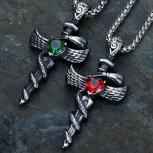 Può includere: Due collane con pendenti argentati. Ogni pendente presenta un design a pugnale con una gemma, una verde e una rossa. I pugnali hanno dettagli di ali e serpenti. Le collane sono su una catena d'argento.