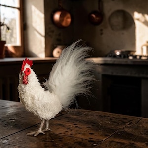 May include: A decorative rooster figurine featuring a textured white body made of fine fibers, a long wispy white tail, and a bright red comb and wattle. The bird stands on two light-colored legs and feet, showcasing a detailed avian design.