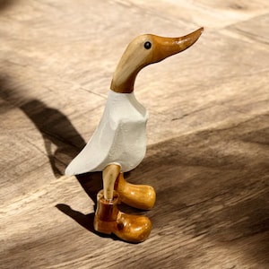 May include: A white wooden duck figurine with brown wooden legs and feet. The duck has a long, brown beak and a black eye.