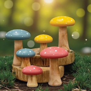 May include: A collection of six wooden mushroom figurines with painted caps. The caps are painted in various colors, including yellow, red, and blue, and feature white polka dots. The mushrooms are displayed on a wooden base, with a blurred green background.