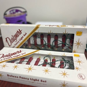 May include: A white box with gold stars and the text "Designers Deluxe Fancy Light Set" on the front. The box contains a set of red and yellow Christmas lights.