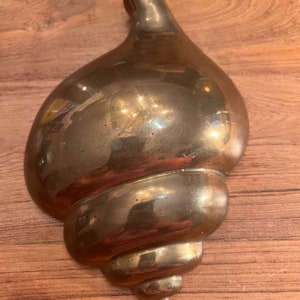 May include: A shiny gold brass seashell sculpture. The shell is detailed with ridges and curves.