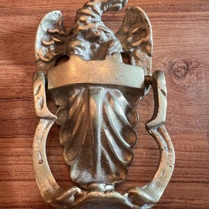 Puede incluir: Un llamador de puerta de latón con forma de águila con las alas extendidas. El águila está posada sobre una base decorativa con una placa rectangular en blanco.