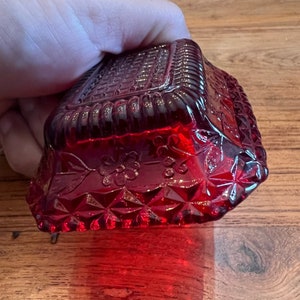 May include: A red glass dish with a diamond pattern and floral design. The dish has a raised rim and a textured surface.