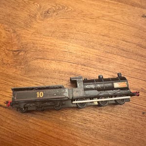 Op de afbeelding: Een zwarte speelgoedtrein met een kolenwagen. Het nummer 10 is zichtbaar op de kolenwagen en de naam "Atlas" staat op de locomotief. De trein staat op een houten oppervlak.