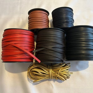 Puede incluir: Un surtido de carretes de cordón de cuero en varios colores, incluyendo rojo, marrón, negro y dorado. Los carretes están apilados, mostrando las diferentes tonalidades y texturas del cuero. Los cordones son planos y parecen adecuados para manualidades o joyería. Medidas en centímetros.