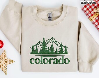 Può includere: Felpa beige con ricamo verde raffigurante montagne e foreste. La parola "colorado" è ricamata in verde sotto il disegno. La felpa è realizzata in materiale morbido, ideale per attività all'aperto.