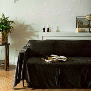 May include: A dark brown velvet sofa with a book and a tray on the seat. The sofa is in front of a white wall with a shelf above it.