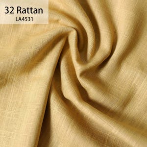 Puede incluir: Primer plano de una tela texturizada de color amarillo dorado con patrones de tejido visibles. La tela est&aacute; drapeada en pliegues suaves, creando sombras y reflejos. El texto "32 Rattan" y "LA4531" est&aacute; en la esquina superior izquierda.