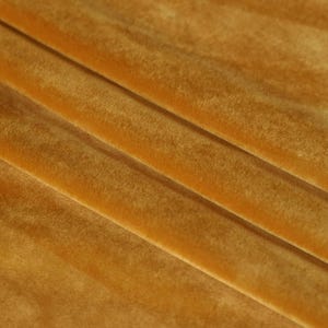 May include: Close-up of a soft, golden yellow velvet fabric. The fabric has a subtle sheen and a smooth, luxurious texture.