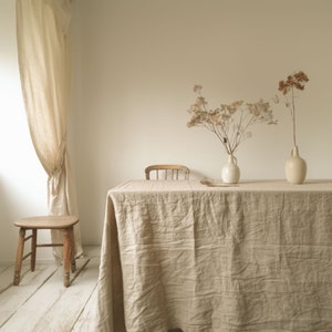 May include: A light brown linen tablecloth draped over a wooden table with a wooden chair and a small wooden stool. Two vases with dried flowers are on the table.