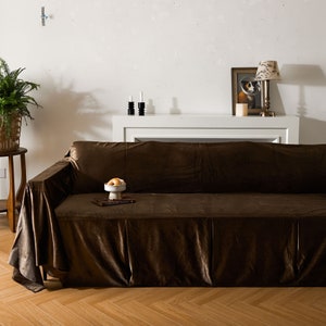 May include: A brown velvet sofa with a matching throw blanket. The sofa is in a living room setting with a white mantelpiece above it.