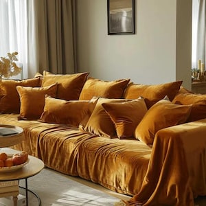 May include: A large, plush, mustard yellow velvet sofa with multiple throw pillows. The sofa is covered in a matching throw blanket.